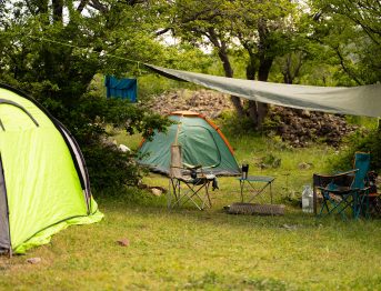 Two tourist camping tents with chairs and table in nature with green forest and grass among a trees on a background, eco tourism and outdoor equipment for hiking; Shutterstock ID 2650862087; purchase_order: -; job: -; client: -; other: